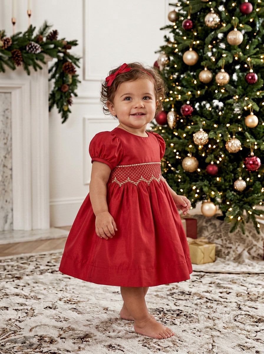 Carriage Boutique red taffeta baby dress with smocked diamond detailing and puffed sleeves near a Christmas tree