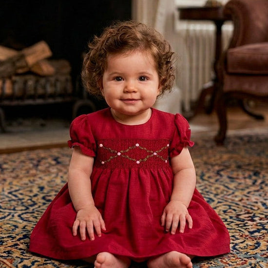 Carriage Boutique baby girl wearing a red short sleeve silk dress with smocked floral detail and puffy sleeves.