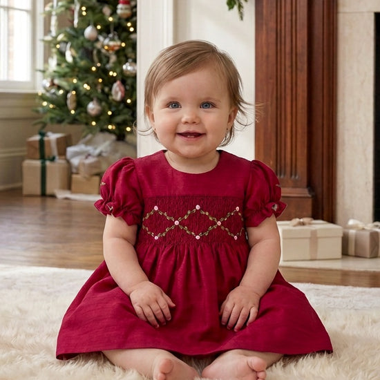 Carriage Boutique red silk baby dress with smocked floral detail and puffy sleeves worn by a toddler in a home setting