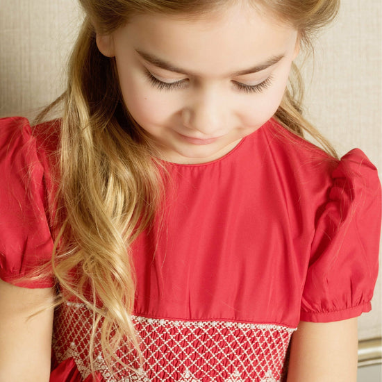 Carriage Boutique toddler girl in a red taffeta dress with smocked diamond detailing and puffed sleeves