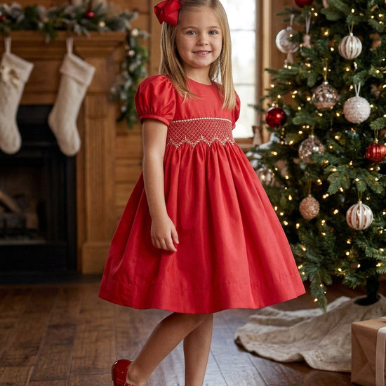 Carriage Boutique toddler girl in a red taffeta dress with smocked bodice, puffed sleeves, and matching hair bow.