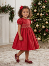 Carriage Boutique toddler girl in a red taffeta dress with smocked diamond detailing and puffed sleeves by a tree