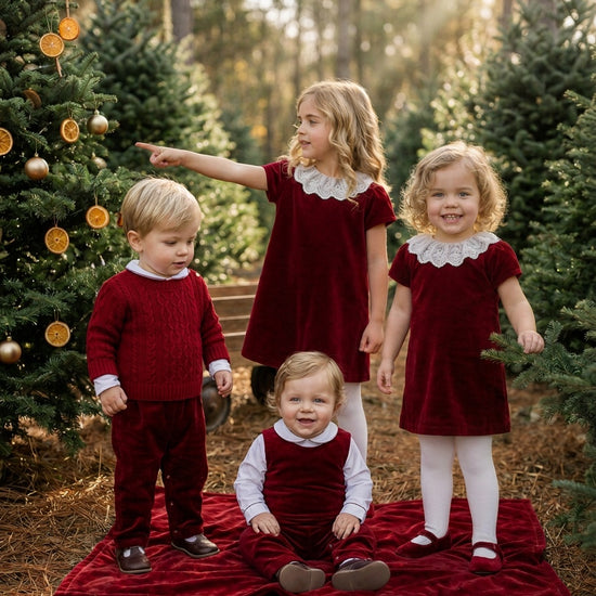 Carriage Boutique toddler girls wearing red velvet dresses with white lace collars posing in a festive forest setting
