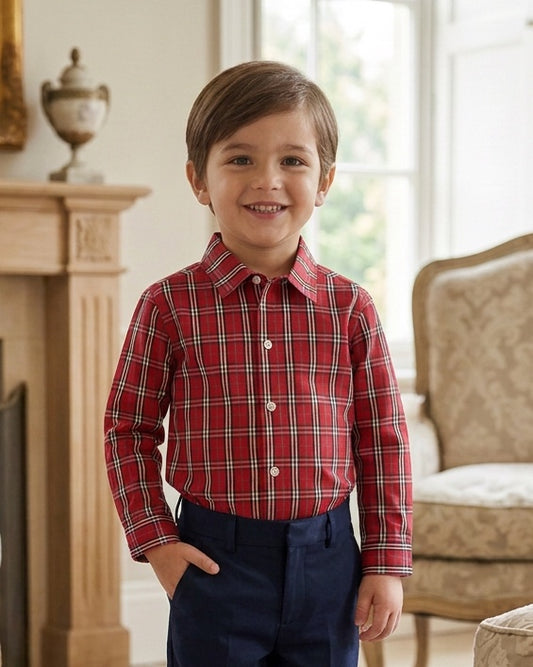 A young boy smiling while wearing a Carriage Boutique red and white plaid long sleeve cotton shirt with navy pants.