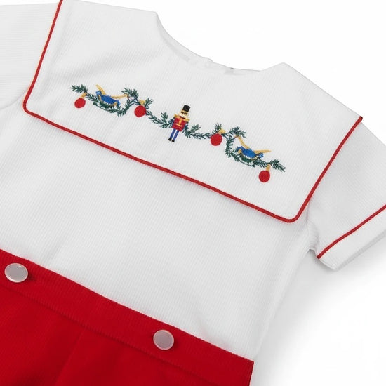 Carriage Boutique white cotton bobbie suit with red trim and smocked bib featuring a wooden soldier and nutcracker embroidery.