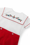 Carriage Boutique white cotton bobbie suit with red trim and smocked bib featuring a wooden soldier and nutcracker embroidery.