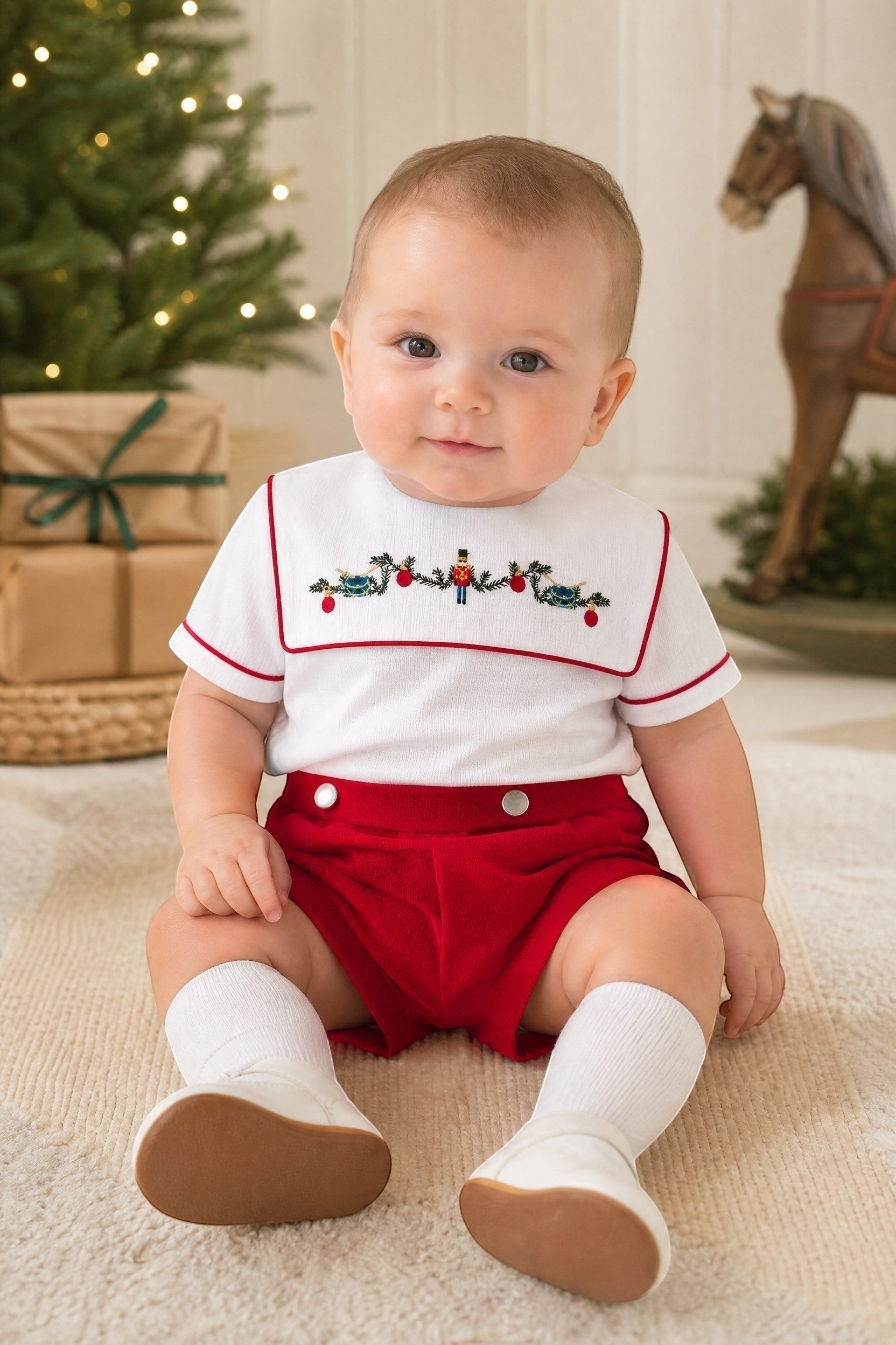 Carriage Boutique red wooden soldier smocked bib, white cotton shirt with red trim, and red shorts. Infant boy outfit.