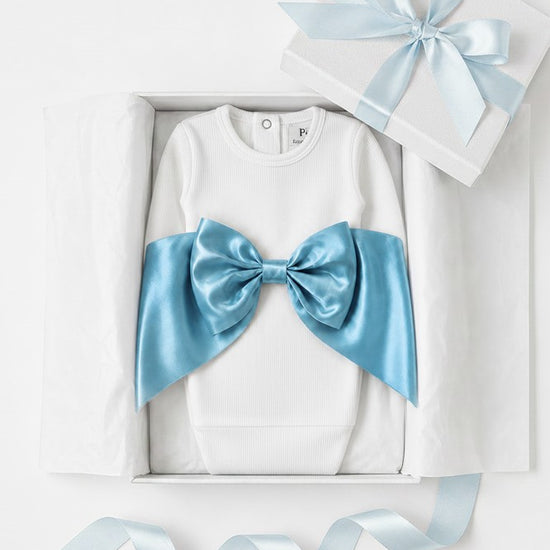 Carriage Boutique white ribbed newborn sleep sack with a large shimmering blue satin bow inside a gift box.