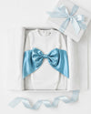 Carriage Boutique white ribbed newborn sleep sack with a large shimmering blue satin bow inside a gift box.