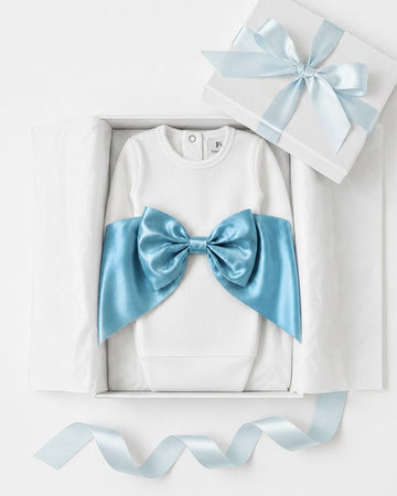 Carriage Boutique white ribbed newborn sleep sack with a large shimmering blue satin bow inside a gift box.
