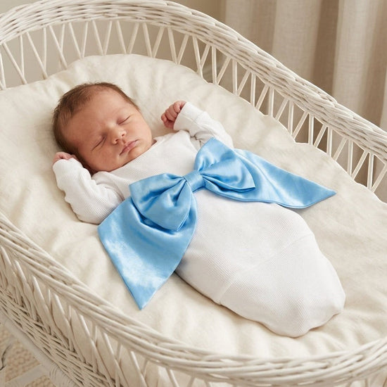 Carriage Boutique white ribbed newborn sleep sack featuring a large shimmering blue satin bow, worn by a sleeping baby.