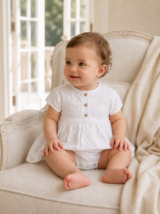 Carriage Boutique white baby girl dress with delicate rosebud print, cap sleeves, and wooden buttons on a seated baby.