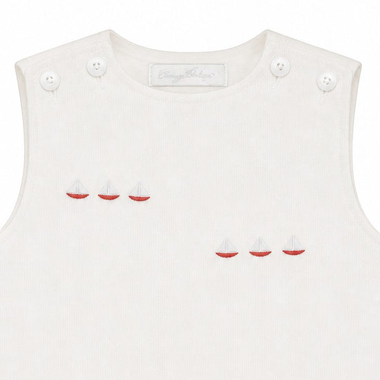 Carriage Boutique white sleeveless baby bubble with smocked detailing and embroidered red sailboats. Button closure.