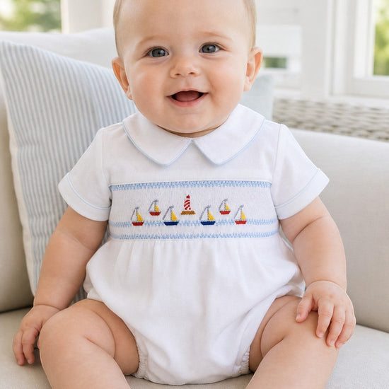 Carriage Boutique white bubble romper with smocked chest featuring sailboats and lighthouse, Peter Pan collar with blue piping.