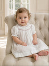 Baby girl wearing a Carriage Boutique off-white smocked dress with black polka dots and floral embroidery