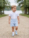 Carriage Boutique toddler boy wearing a white smocked shirt and light blue shorts bobby suit on a gravel path
