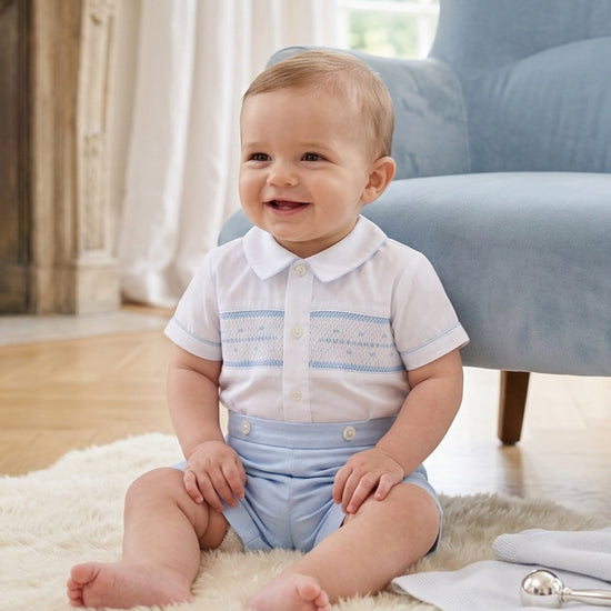 Carriage Boutique baby boy wearing a white button-down shirt with blue hand smocking and light blue shorts