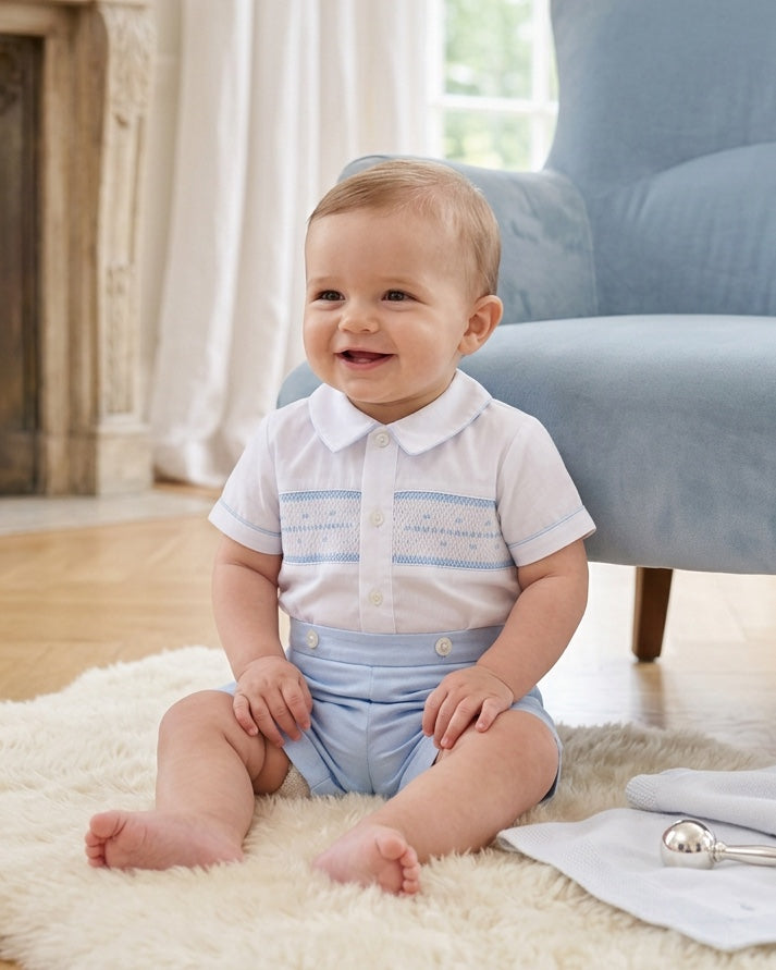 Carriage Boutique baby boy wearing a white button-down shirt with blue hand smocking and light blue shorts