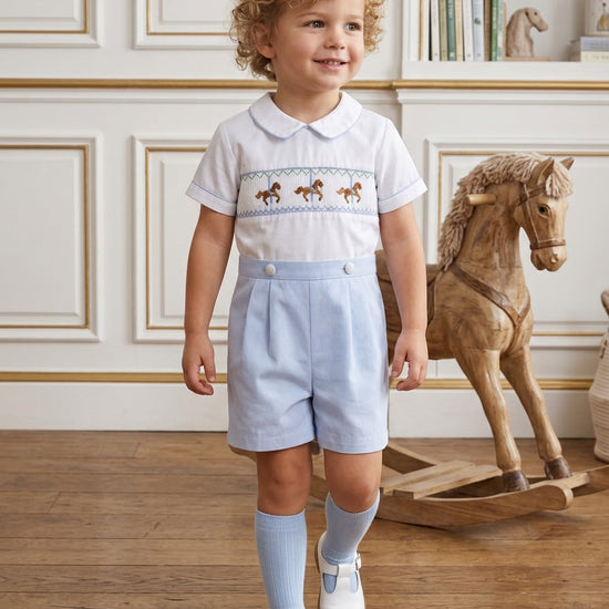 Carriage Boutique baby boy wearing a white and light blue smocked bobby suit with carousel horse embroidery