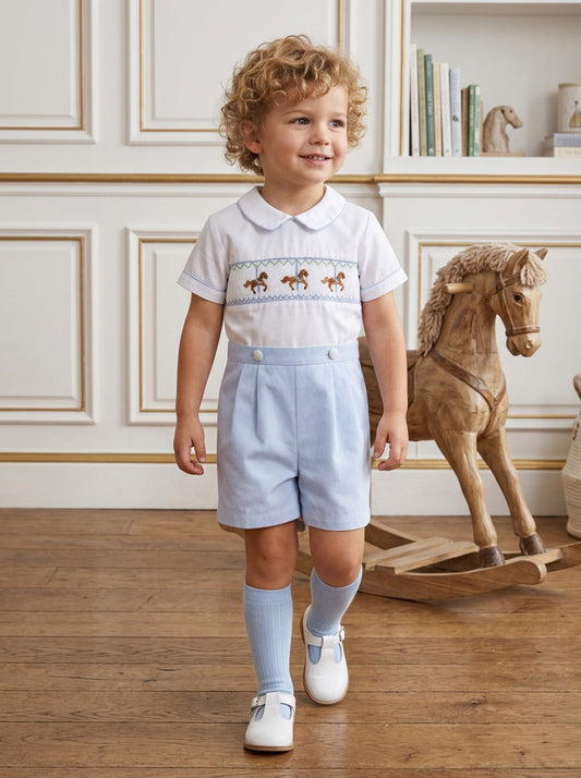 Carriage Boutique baby boy wearing a white and light blue smocked bobby suit with carousel horse embroidery