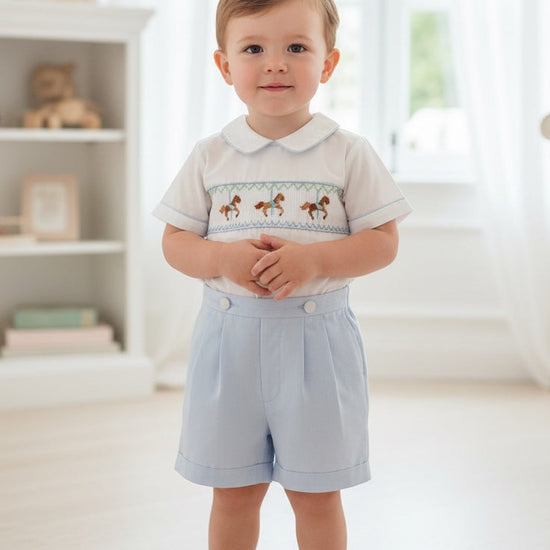 Carriage Boutique toddler boy wearing a white and light blue smocked bobby suit with carousel horse embroidery