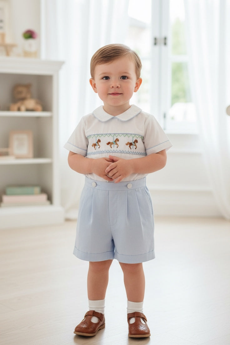Carriage Boutique toddler boy wearing a white and light blue smocked bobby suit with carousel horse embroidery