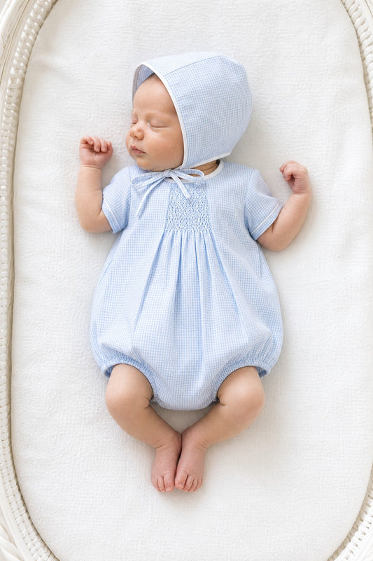 Carriage Boutique light blue gingham smocked bubble and bonnet set with white piping. Baby lying down.