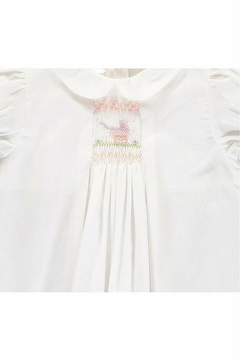 Carriage Boutique white baby dress with hand-smocked bodice, pastel pram embroidery, and Peter Pan collar.