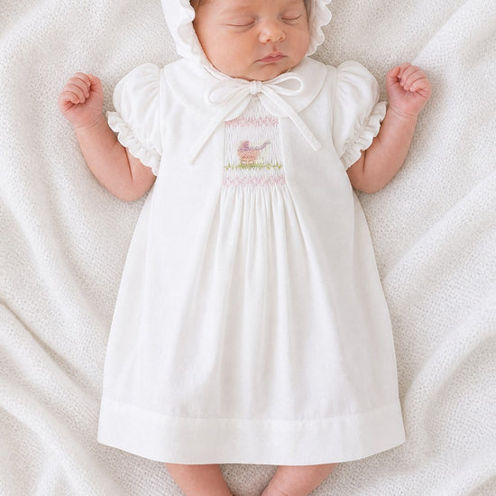 Carriage Boutique white smocked heirloom dress and ruffled bonnet set on a sleeping baby with pram embroidery.