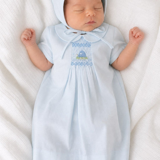 Newborn baby wearing a Carriage Boutique baby blue smocked heirloom dress and matching bonnet on a white blanket.
