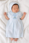Newborn baby wearing a Carriage Boutique baby blue smocked heirloom dress and matching bonnet on a white blanket.