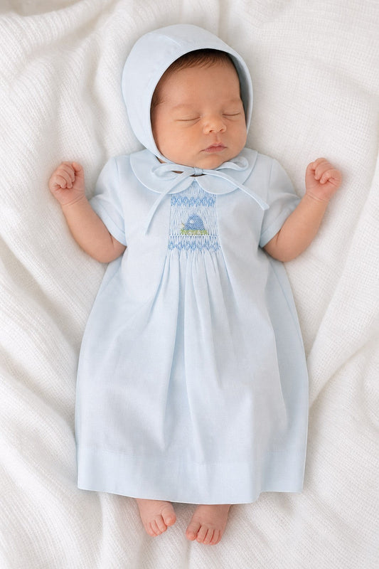 Newborn baby wearing a Carriage Boutique baby blue smocked heirloom dress and matching bonnet on a white blanket.