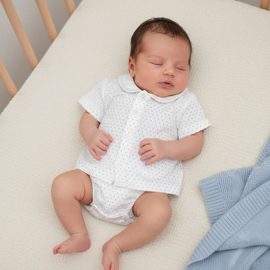 Newborn baby boy sleeping in a Carriage Boutique white cotton shirt and diaper cover set with grey star embroidery.