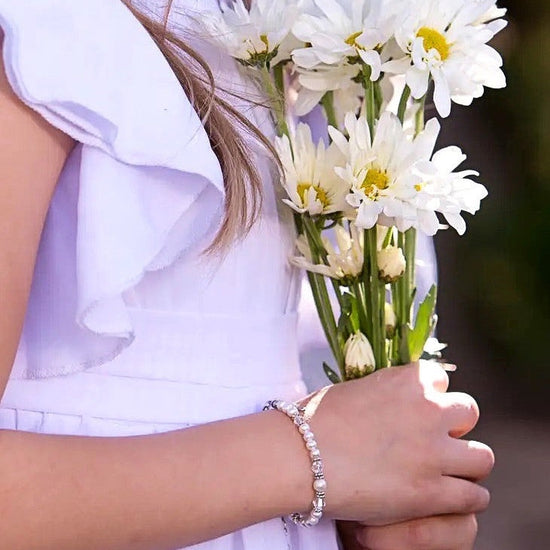 Carriage Boutique sterling silver cross bracelet with freshwater pearls and crystals worn by a girl holding daisies.
