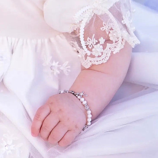 Carriage Boutique sterling silver baby cross bracelet with freshwater pearls on a baby wearing a lace christening gown