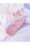 Carriage Boutique sterling silver baby cross bracelet with freshwater pearls on a baby wearing a lace christening gown