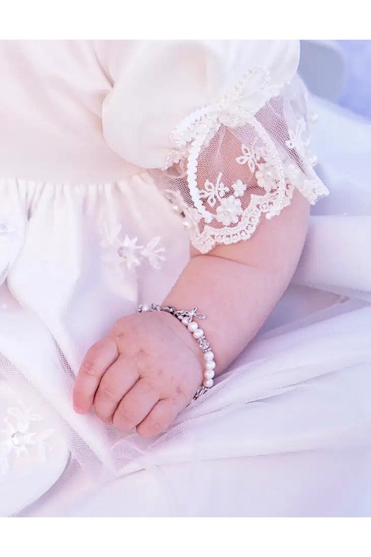Carriage Boutique sterling silver baby cross bracelet with freshwater pearls on a baby wearing a lace christening gown