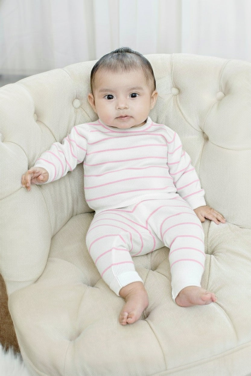 Baby wearing a Carriage Boutique white and blush pink striped cotton long-sleeve legging set while sitting on a chair.