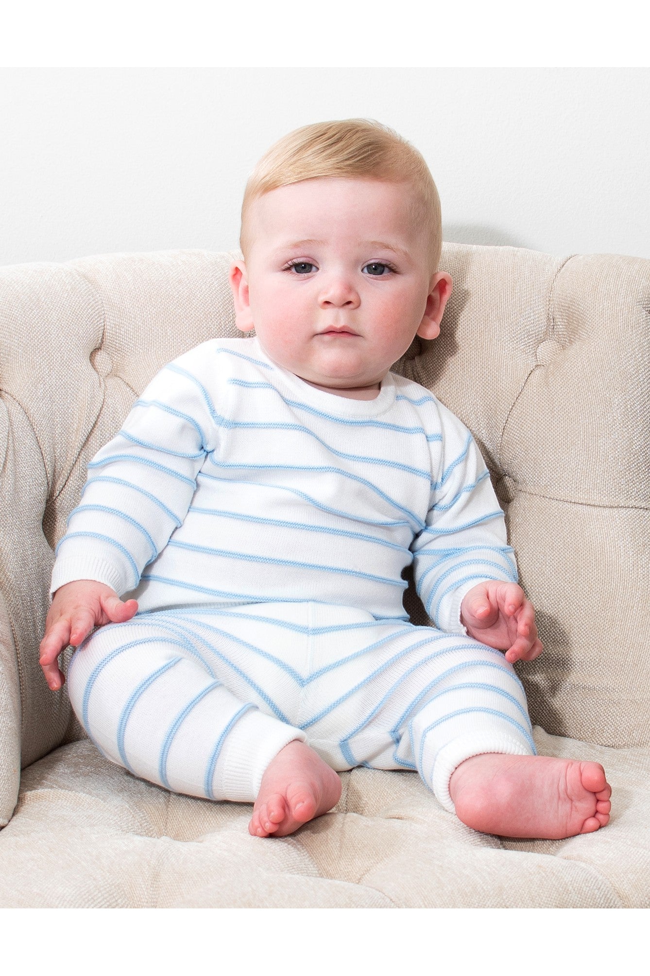 Baby wearing a Carriage Boutique white and sky-blue striped long-sleeve top and legging set while sitting in a chair.