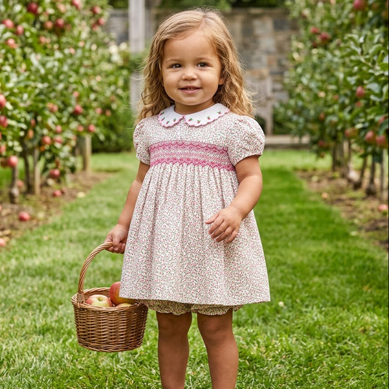 Carriage Boutique toddler girl wearing a tan floral cotton dress with smocked red diamond detail and puff sleeves.