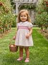 Carriage Boutique toddler girl wearing a tan floral cotton dress with smocked red diamond detail and puff sleeves.
