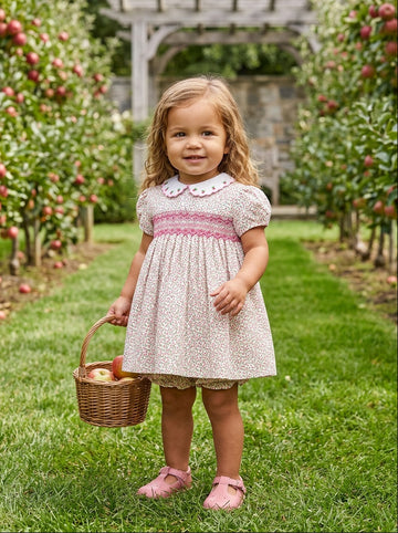 Carriage Boutique toddler girl wearing a tan floral cotton dress with smocked red diamond detail and puff sleeves.
