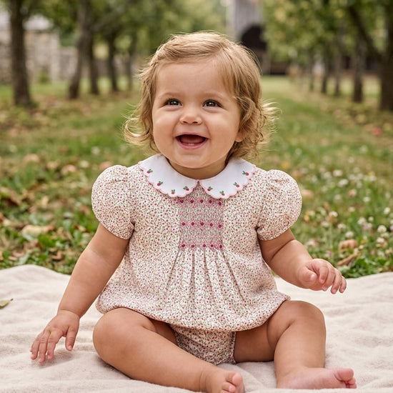 Carriage Boutique baby girl wearing a tan floral puff sleeve bubble romper with pink smocked diamond detailing.