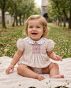 Carriage Boutique baby girl wearing a tan floral puff sleeve bubble romper with pink smocked diamond detailing.