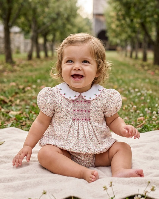 Carriage Boutique baby girl wearing a tan floral puff sleeve bubble romper with pink smocked diamond detailing.