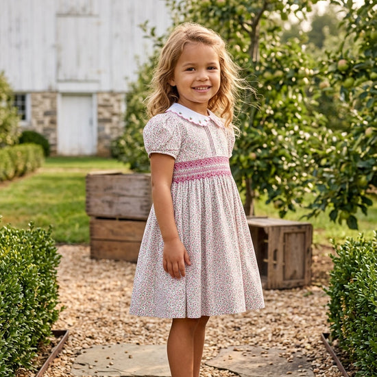 Carriage Boutique toddler girl wearing a tan floral cotton dress with puff sleeves and smocked red diamond detailing.