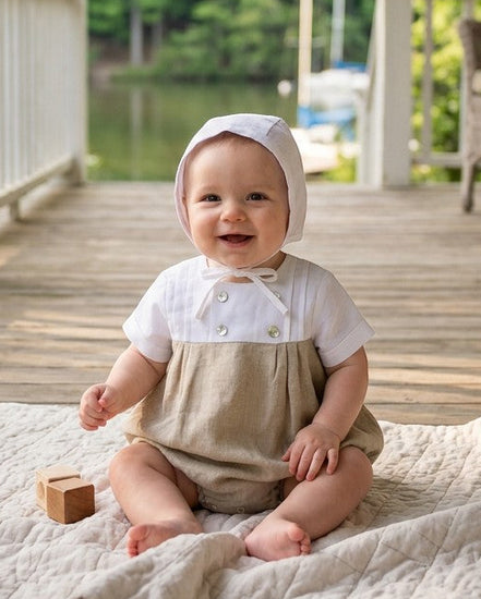 A happy baby boy wearing a Carriage Boutique tan and white bubble romper with a matching bonnet on a porch.