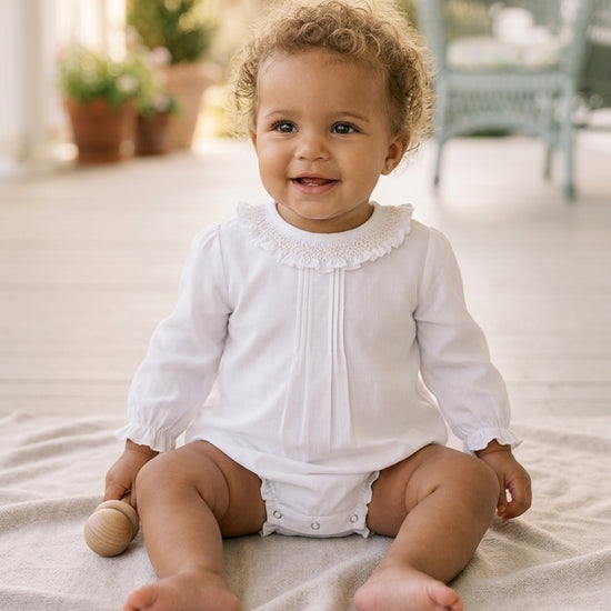 Carriage Boutique baby girl white long sleeve bubble romper with smocked collar sitting on a soft blanket