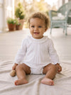 Carriage Boutique baby girl white long sleeve bubble romper with smocked collar sitting on a soft blanket