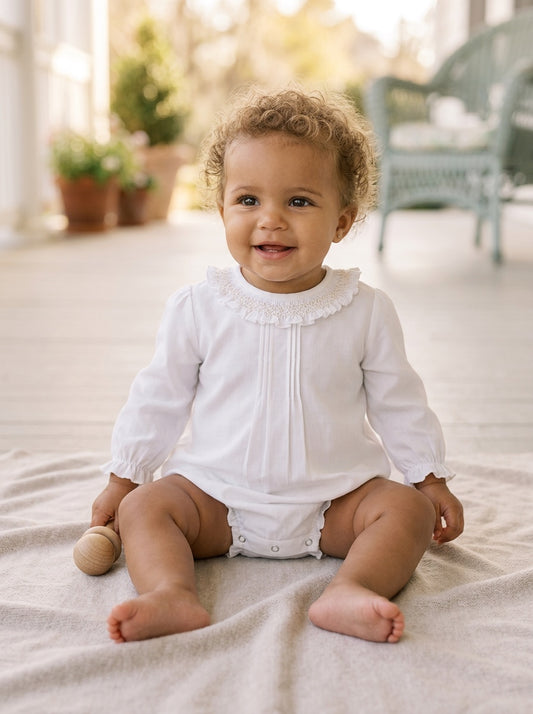 Carriage Boutique baby girl white long sleeve bubble romper with smocked collar sitting on a soft blanket